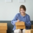 Woman packing boxes for shipping, sitting on a couch in a cozy living room