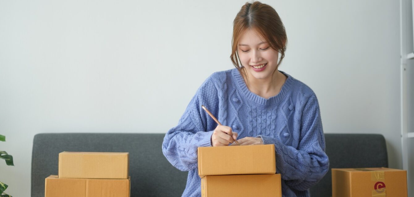 woman-packing-boxes-for-shipping-sitting-on-a-couch-in-a-cozy-living-room woman-packing-boxes-for-shipping-sitting-on-a-couch-in-a-cozy-living-room